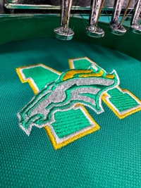 a green logo with a sports team logo on, under an embroidery machine